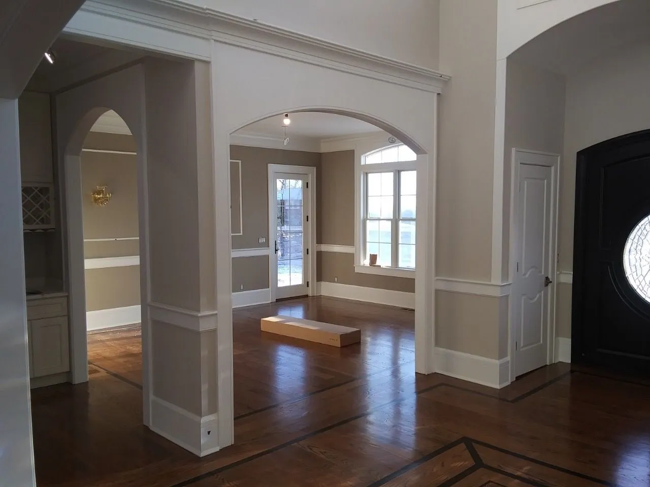 Empty living room with hardwood floors, arched openings, and large windows letting in daylight
