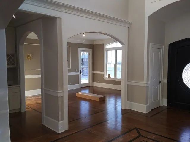 Empty living room with hardwood floors, arched openings, and large windows letting in daylight