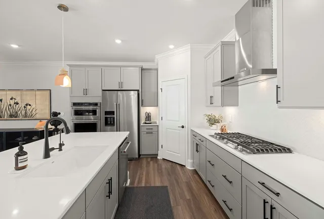 Bright modern kitchen with white cabinets, gray drawers, island, stainless steel appliances, and wood floors